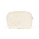 A cream-colored faux fur cosmetic pouch with a small silver zipper pull and a circular embossed logo on the front, set against a plain white background.