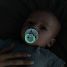 Baby with a glowing pacifier in a dark setting