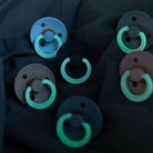 Multiple pacifiers with green rings on a dark background