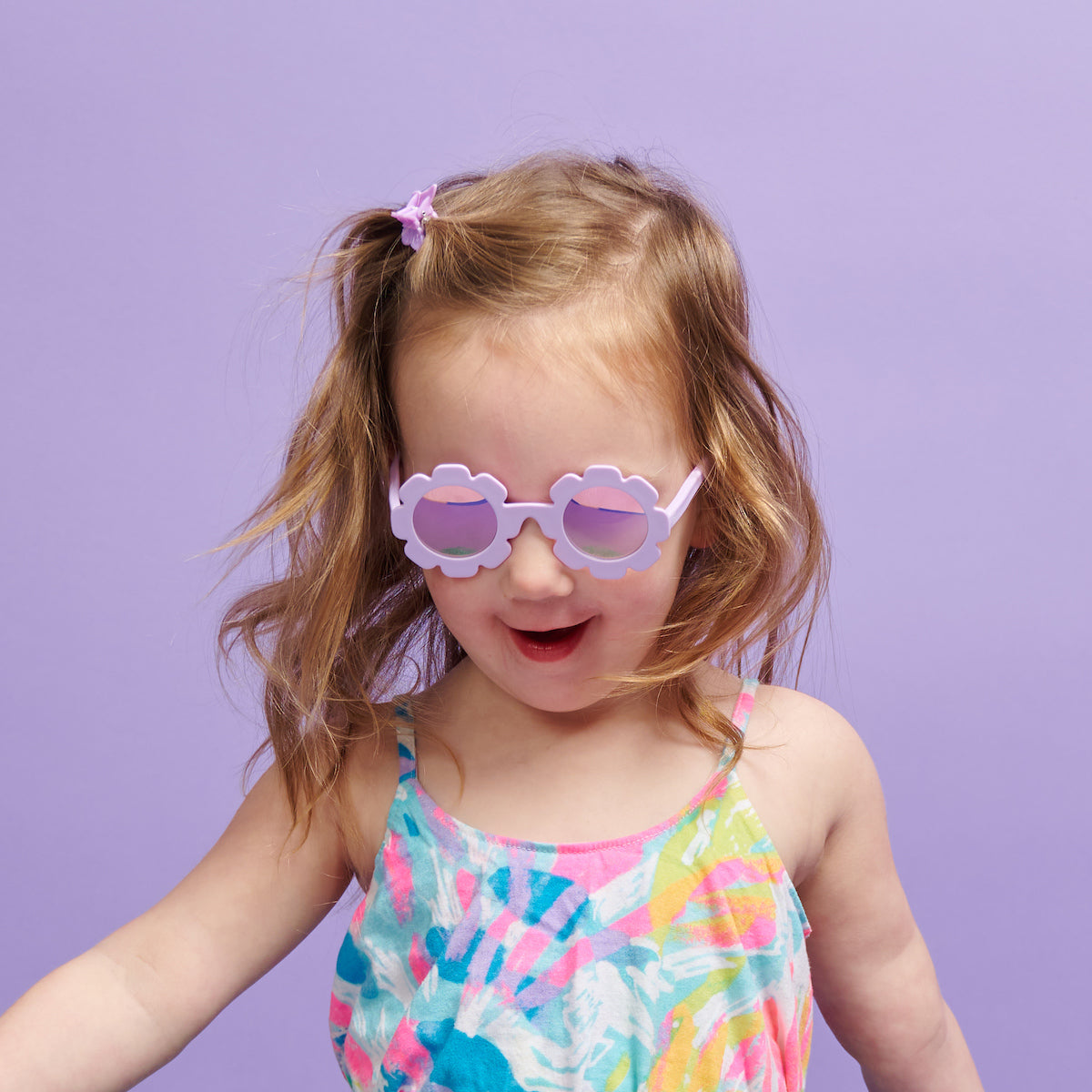Child wearing colorful sunglasses and a swimsuit against a purple background
