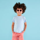 Child wearing sunglasses and a light blue shirt with pink pants on a blue background
