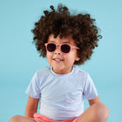 Child wearing pink sunglasses and a light blue shirt against a blue background