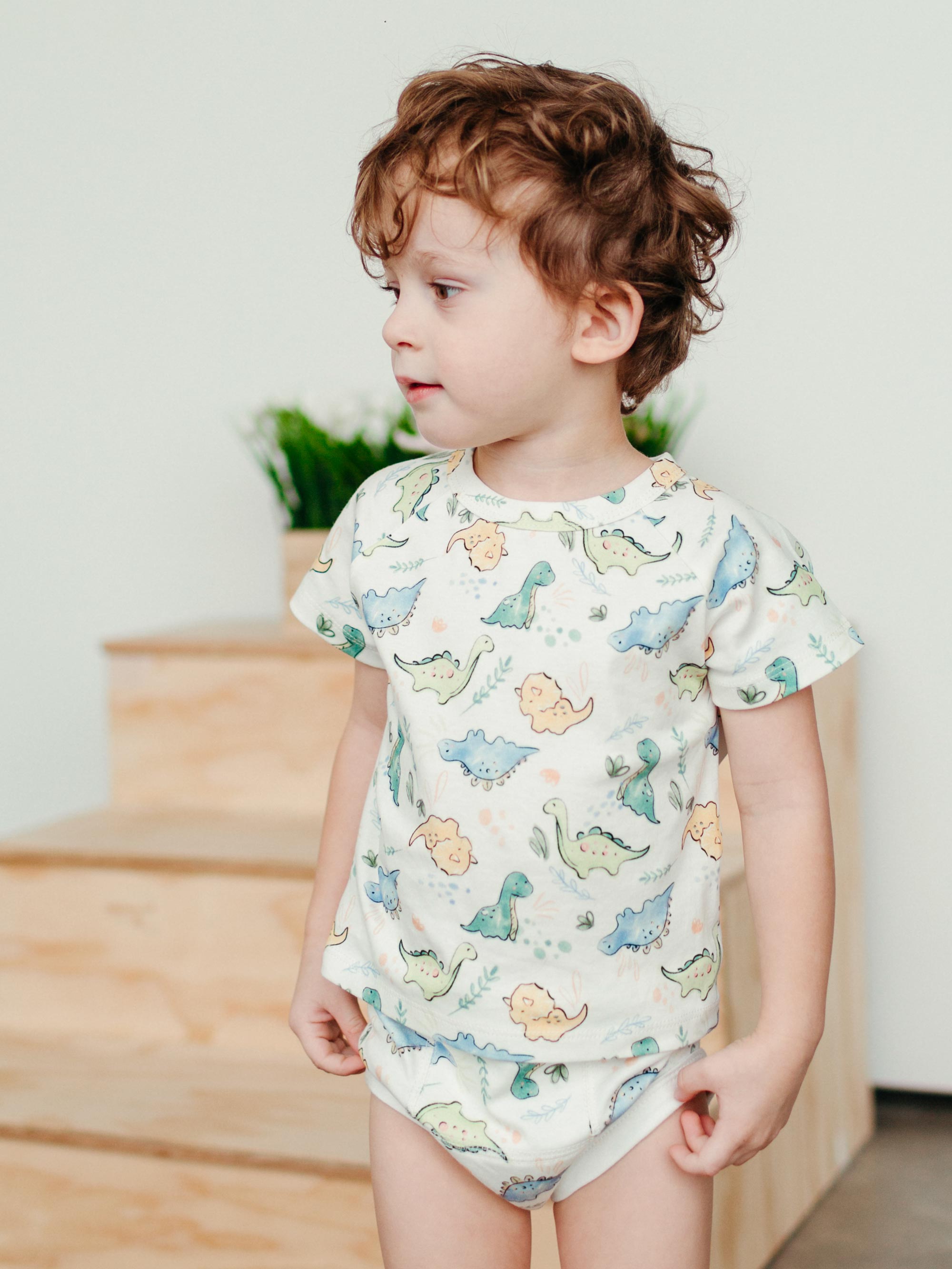 Child wearing a dinosaur-patterned onesie indoors.