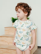 Child wearing a dinosaur-patterned onesie indoors.