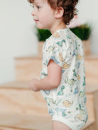 Child wearing a dinosaur-patterned onesie sitting on a wooden floor.
