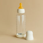 Clear baby bottle with orange nipple and white cap on a beige background