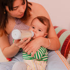 Woman holding a baby and feeding them with a bottle against a neutral background