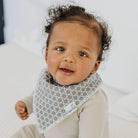 Baby wearing a gray and white patterned bib with a blurred background