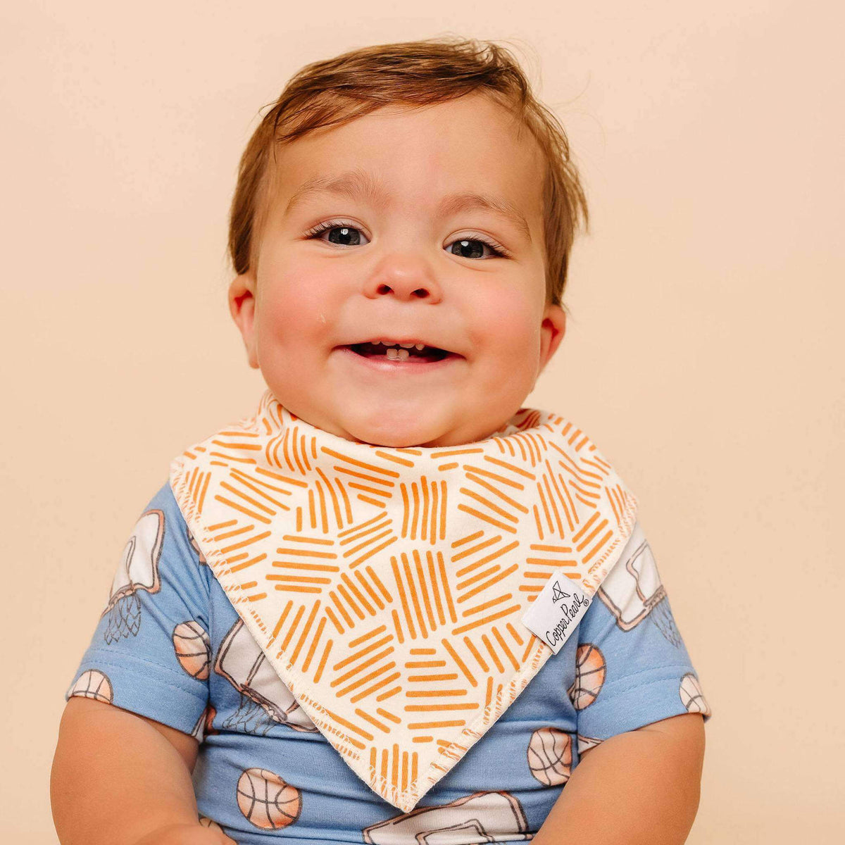 Baby wearing a patterned bib and shirt on a beige background
