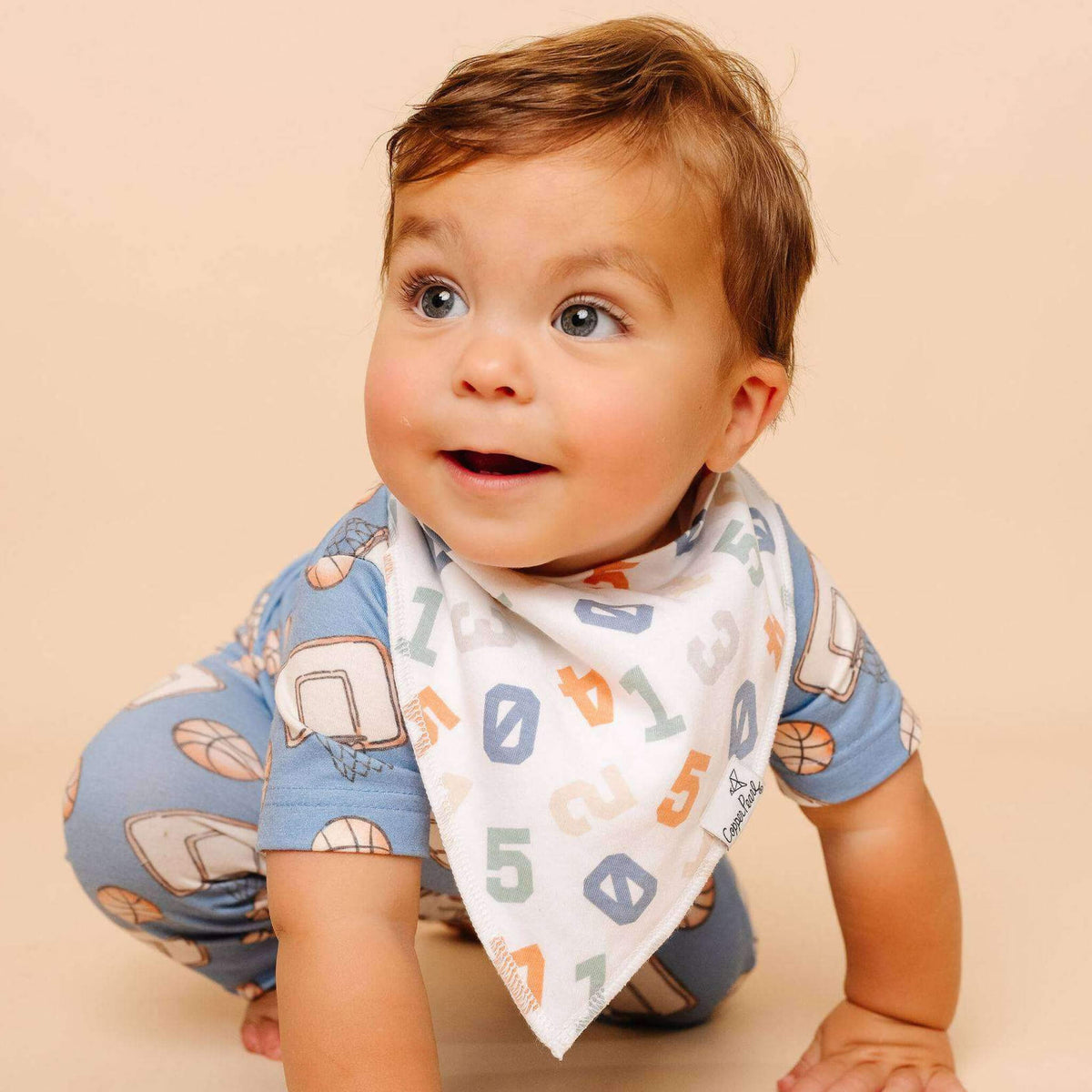 Baby wearing a blue shirt with elephant patterns and a white bib with numbers and letters on a beige background