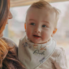 Baby wearing a bib with 'Pooh' branding, held by a person.