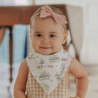 Baby wearing a pink headband and a bib with nature-themed design.