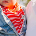 Close-up of a child wearing a red and white striped garment with a brand tag, outdoors.