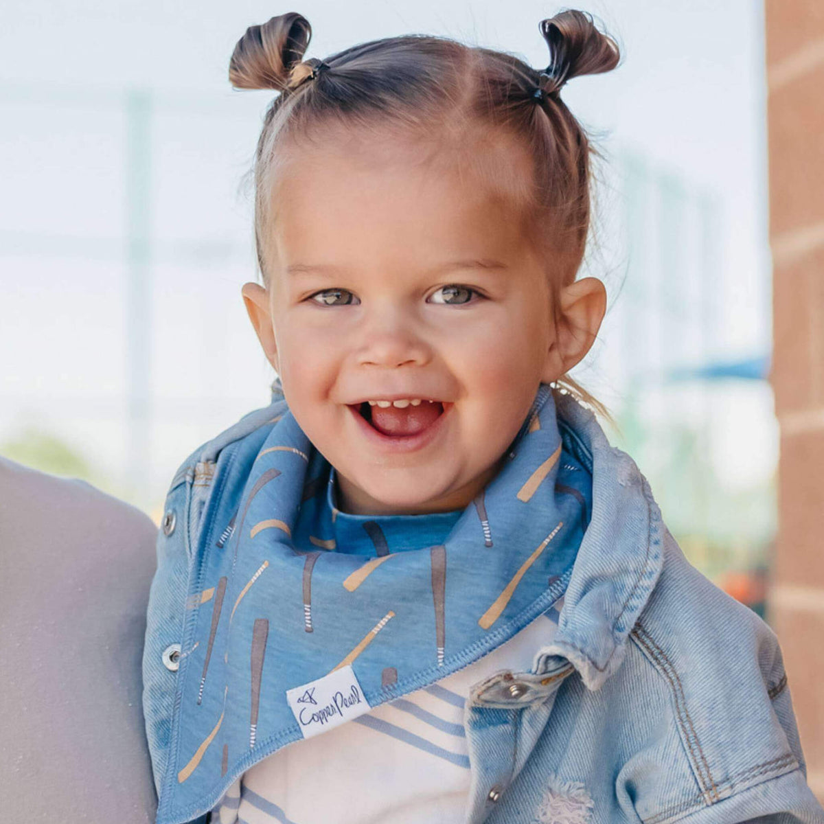 Child wearing a blue denim jacket with a patterned bib, standing outdoors.