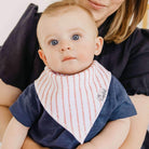 Baby wearing a striped bib with a person holding them, against a neutral background