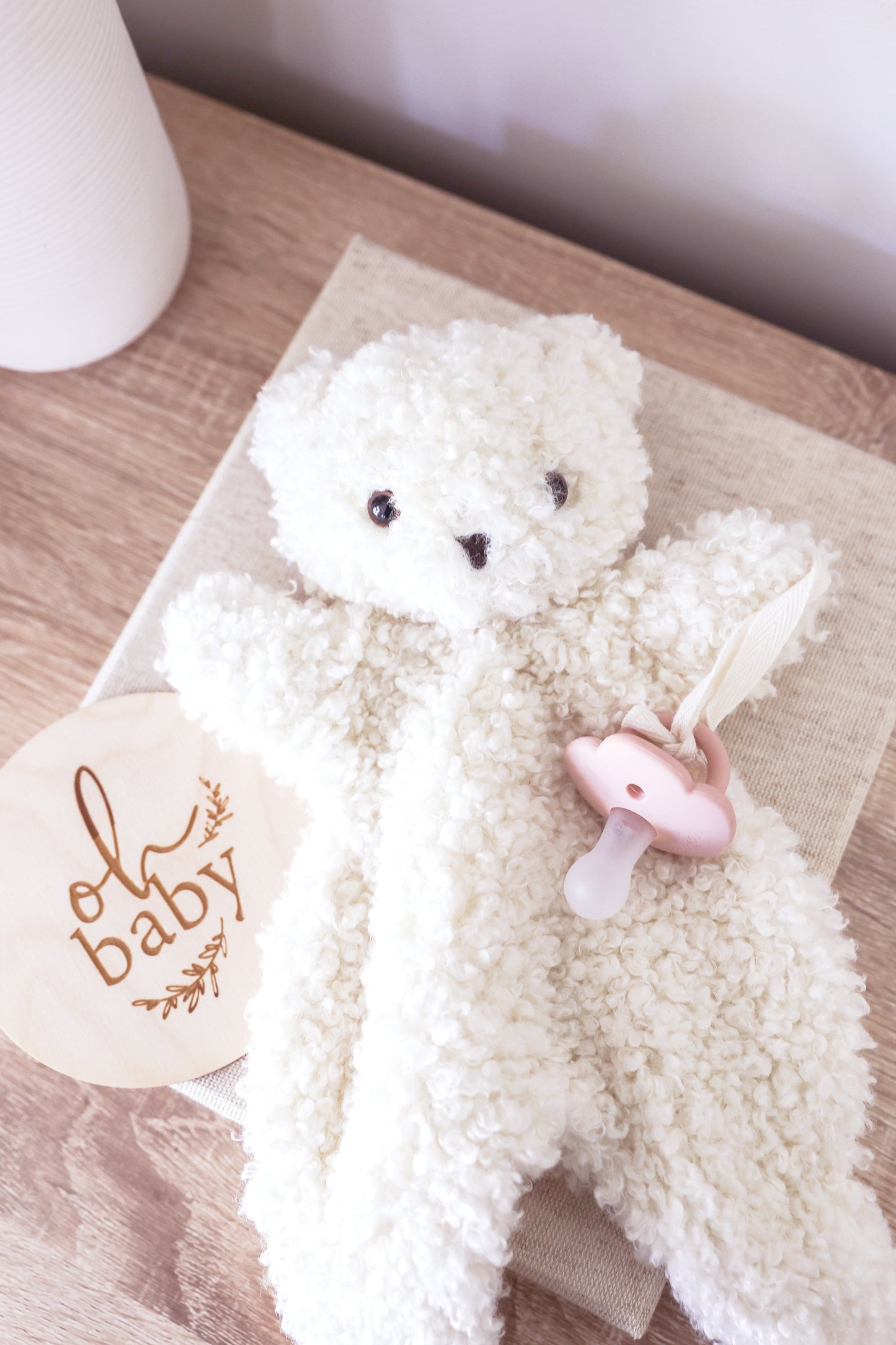 A cream-colored, curly teddy bear plush toy with small black embroidered eyes and nose.