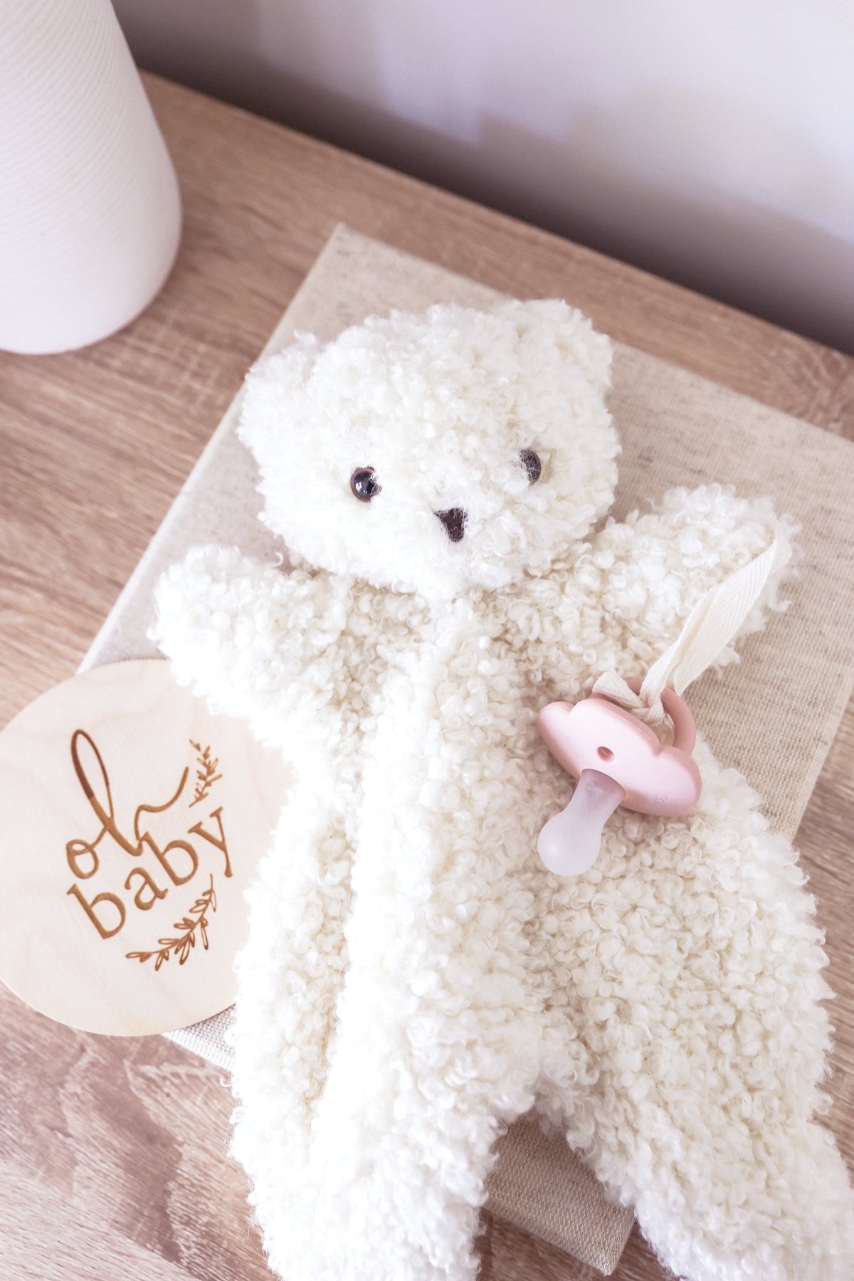 A cream-colored, curly teddy bear plush toy with small black embroidered eyes and nose.