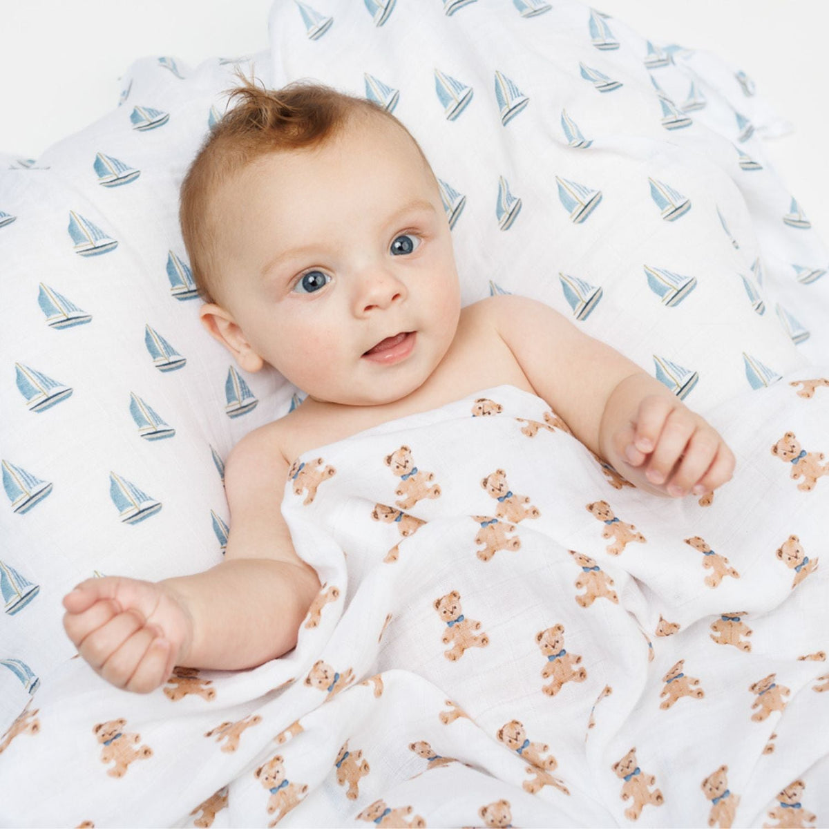 Baby wrapped in a blanket with teddy bear pattern on a sailboat-patterned background
