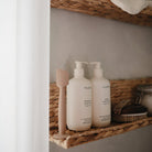 Two white bottles with pump dispensers on a wicker shelf.