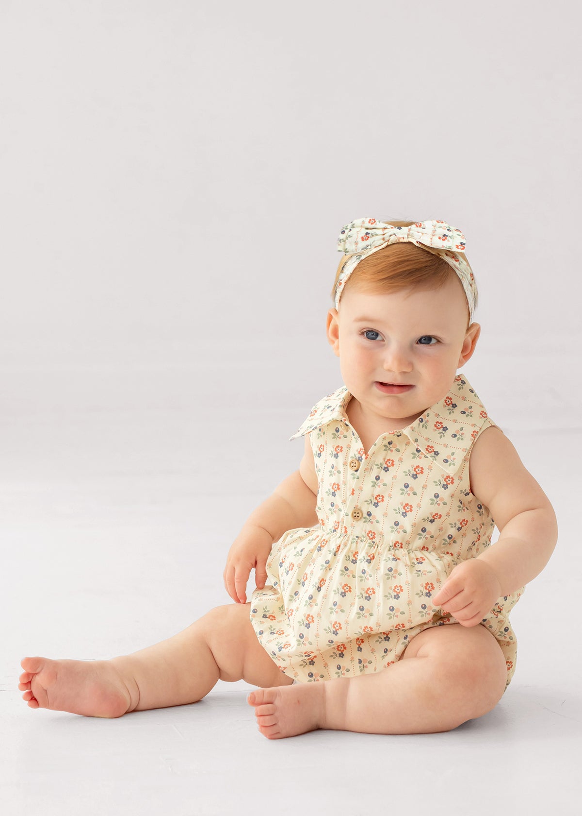 Baby wearing a floral romper and headband on a light gray background