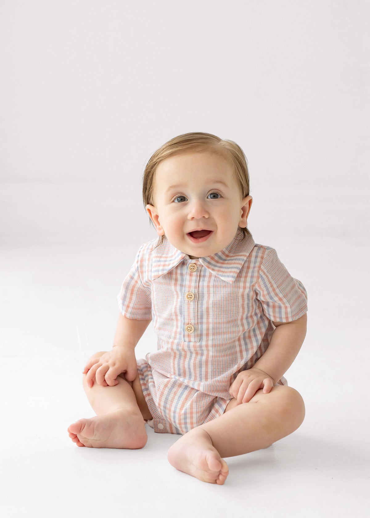 Baby wearing a checkered outfit sitting on a white background