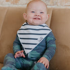 Baby wearing a striped bib and green pajamas sitting on a brown couch.