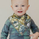 Baby wearing a camouflage-patterned bib and shirt against a plain background