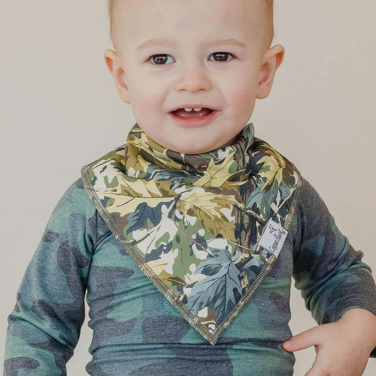 Baby wearing a camouflage-patterned bib and shirt against a plain background