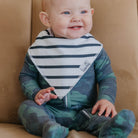 Baby wearing a striped bib and camouflage outfit sitting on a couch.