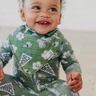 A smiling baby wearing a green long-sleeve one-piece outfit and matching bib with a soccer-themed print, including footballs, hands, and pennants that say GOAL.