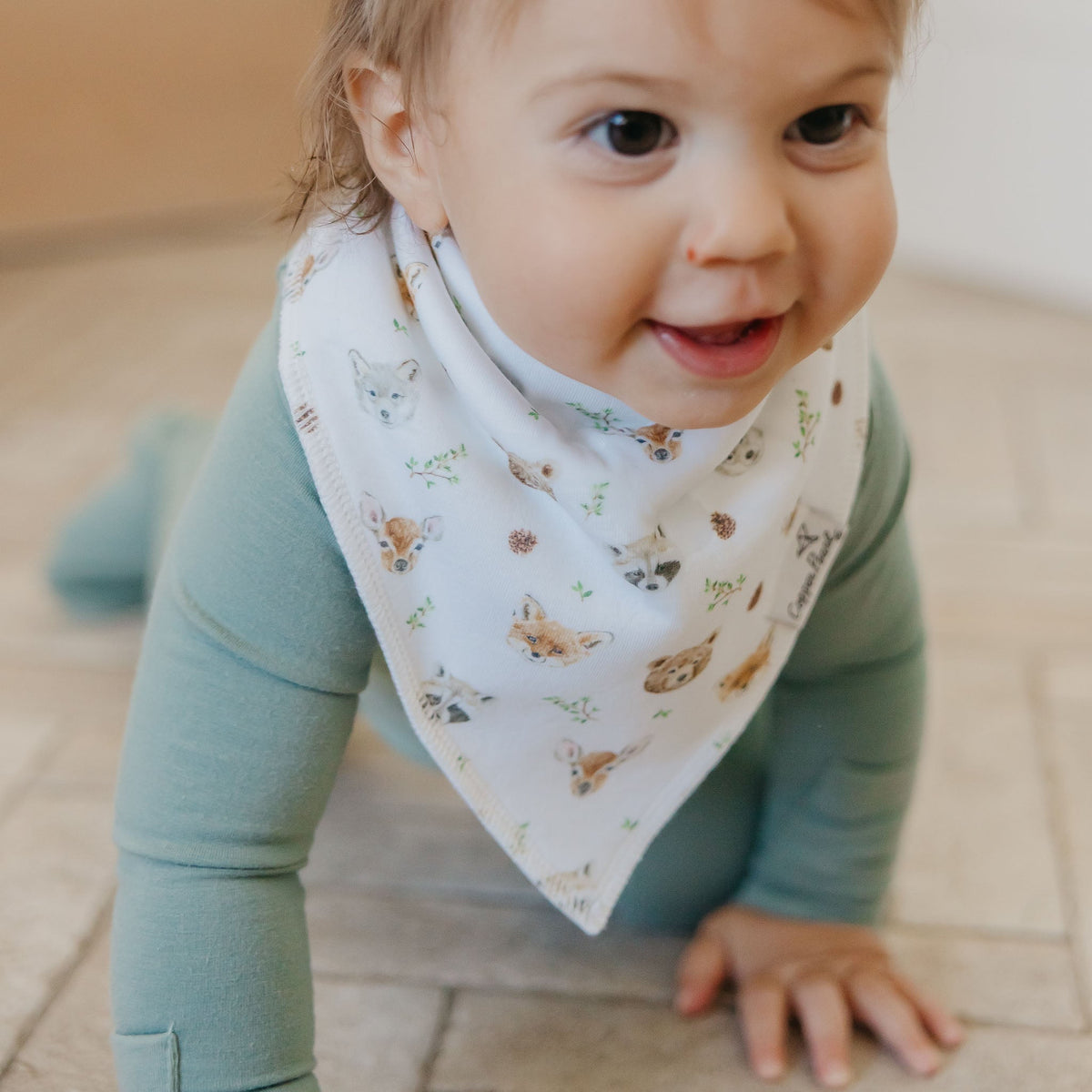 Child wearing a bib with animal patterns on a tiled floor