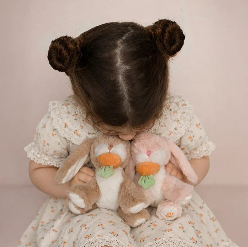 Child holding two plush bunnies with a soft pink background