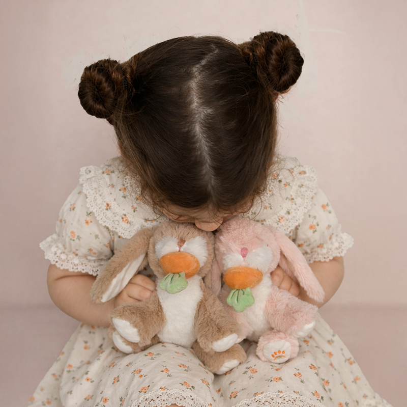 Child holding two plush bunnies against a pink background