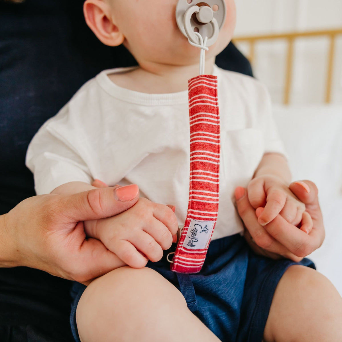 Baby holding a red and white striped teething ring with a blurred background