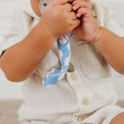 Close-up of a baby's hands holding a blue teething ring with pink patterns.