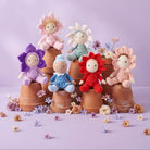 Colorful plush toys resembling flowers and children on terracotta pots with a light purple background.