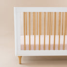 White crib with wooden sides and a pink mattress against a beige background