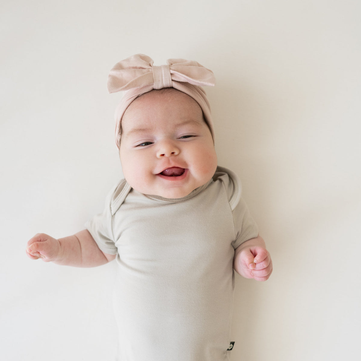 Baby wearing a light gray onesie and pink headband with a bow on a white background