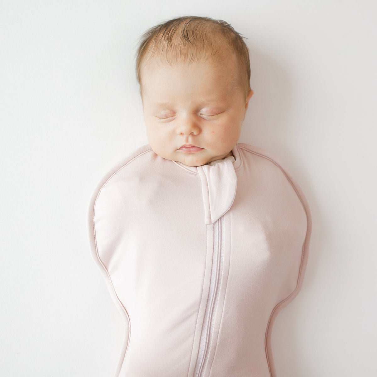 Newborn baby in a pink sleep bag on a white background