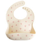 Beige baby bib with red bow pattern on a white background