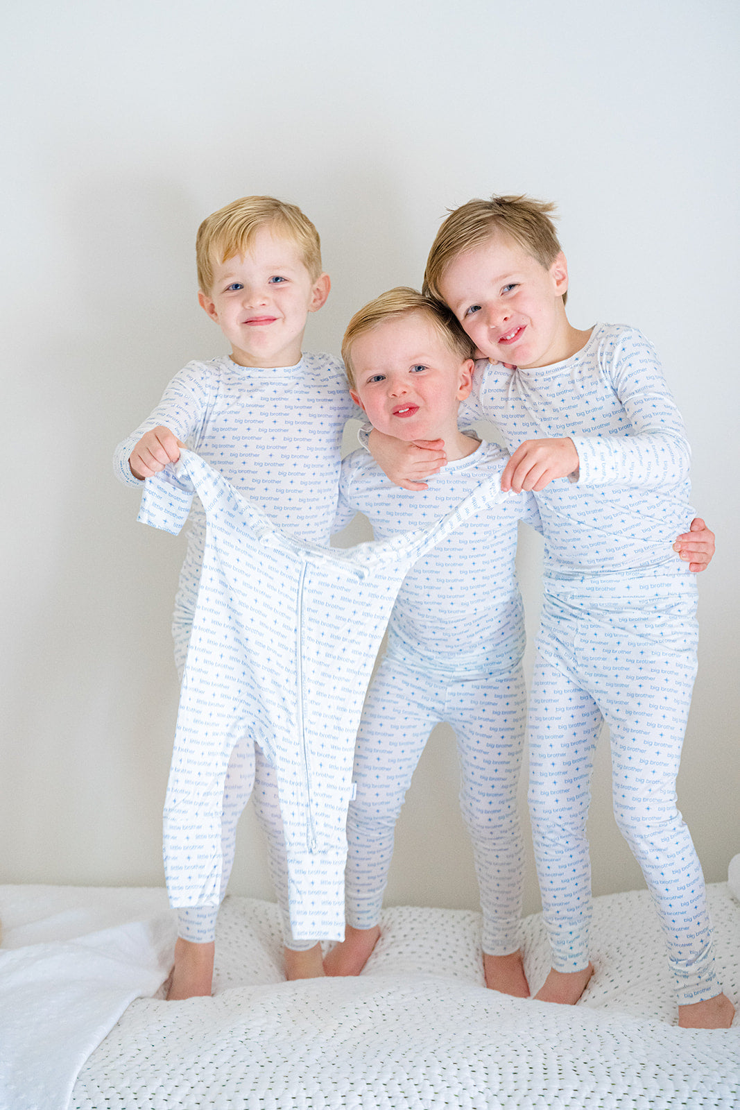 Three children wearing matching pajamas standing on a bed.