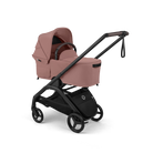 A baby stroller travel system in dusty rose pink and black, shown from a three-quarter angle on a solid white background. The stroller features a pink bassinet, a black frame, and a matching black handlebar.