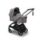 A stroller bassinet attachment in heather gray fabric mounted on a black stroller frame, shown at a three-quarter angle on a clean white background.