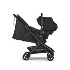 A black stroller and bassinet travel system shown from a side profile view against a solid white background. The stroller features a black fabric liner, a dark gray frame, and black wheels, with a matching black bassinet attached.