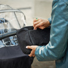 Person holding a black rain cover over a stroller with water droplets on it.