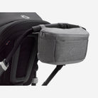 Gray storage basket attached to a black stroller on a white background