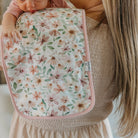 Woman holding a baby wrapped in a floral blanket inside a home.