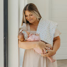 Woman holding a baby wrapped in a floral blanket indoors.