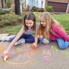 Two young girls playing with sidewalk chalk in a driveway.