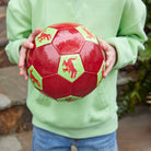 Person holding a red soccer ball with green patterns outdoors